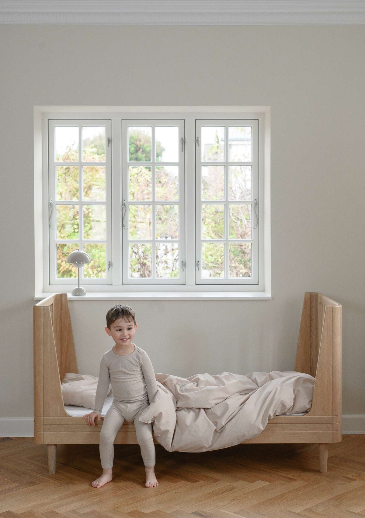 Kind sitzt im We Are Bitte Juniorbett 'Nature Junior Bed 2.0' Eiche 164,5 x 72,5 cm