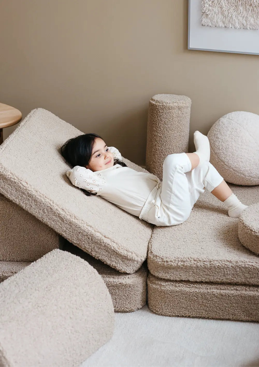 Ein Mädchen liegt entspannt zurückgelehnt auf einer verstellbaren Liegefläche aus den Elementen des modularen Wigiwama Kindersofas Teddy Biscuit.