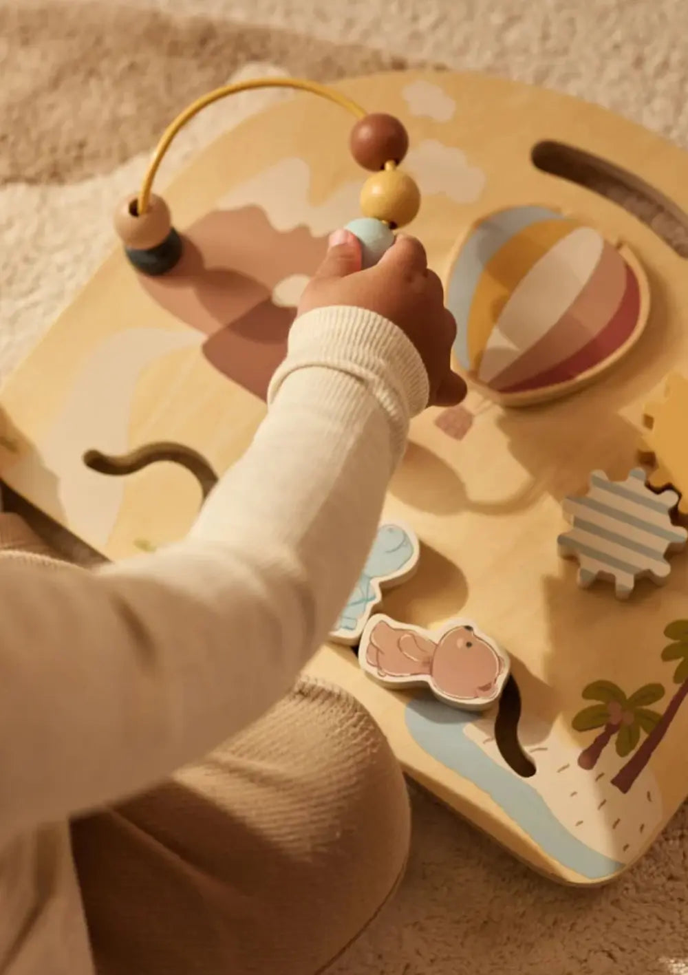 Eine Kinderhand bewegt Holzkugeln auf der Motorikschleife des bunt bedruckten Jollein Holz Aktivitätenboard Jollies.