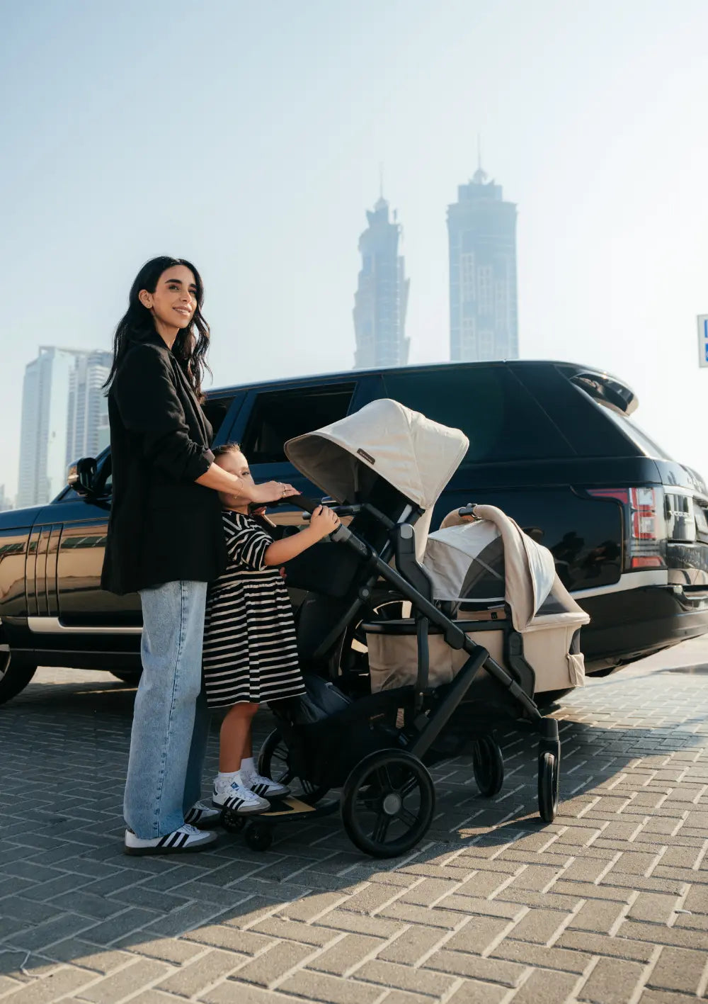 Frau steht mit Kindern im Kinderwagen-Set UPPAbaby 'Vista 3' Liam mit Babywanne,   Sportsitz und Mitfahrbrett vor einem Auto