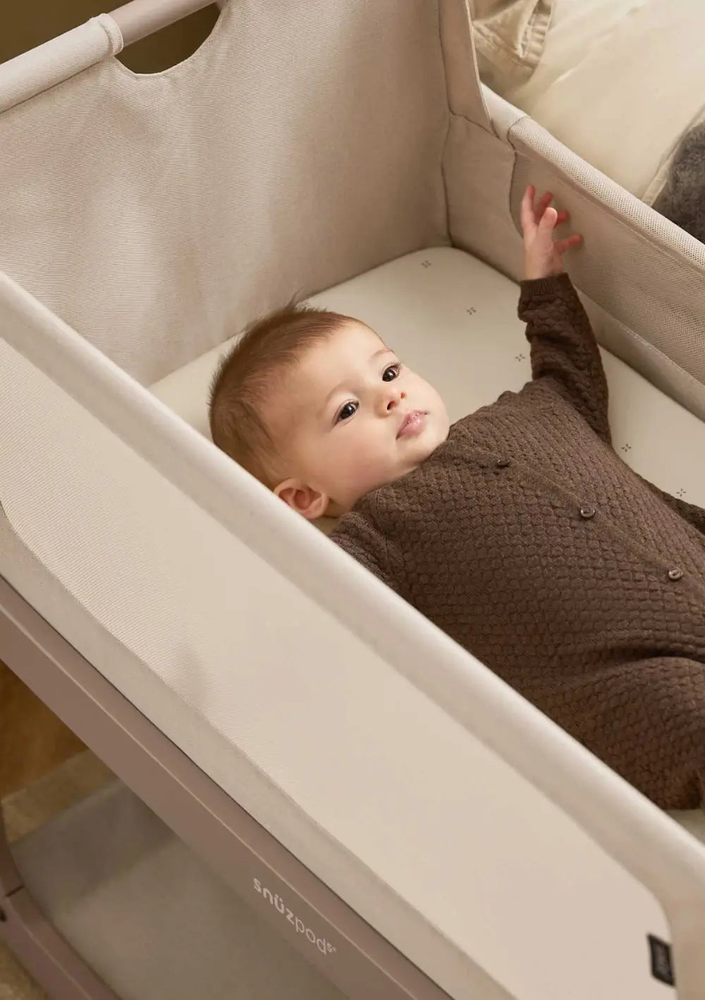 Ein Baby liegt in einem im SnüzPod 5  Beistellbett, das mit dem Spannbettlaken Cashmere mit Kreuzchen bezogen ist.