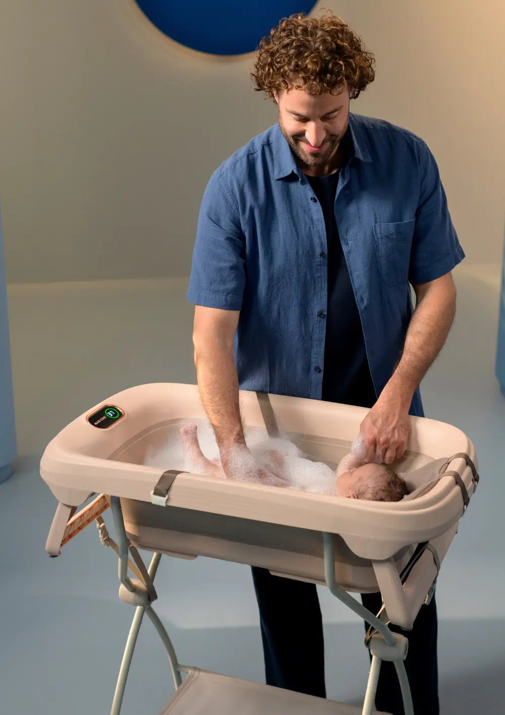 Ein Mann badet sein Baby rückenschonend in der Maxi-Cosi 'Indigo Plus', die auf dem passenden Ständer steht 