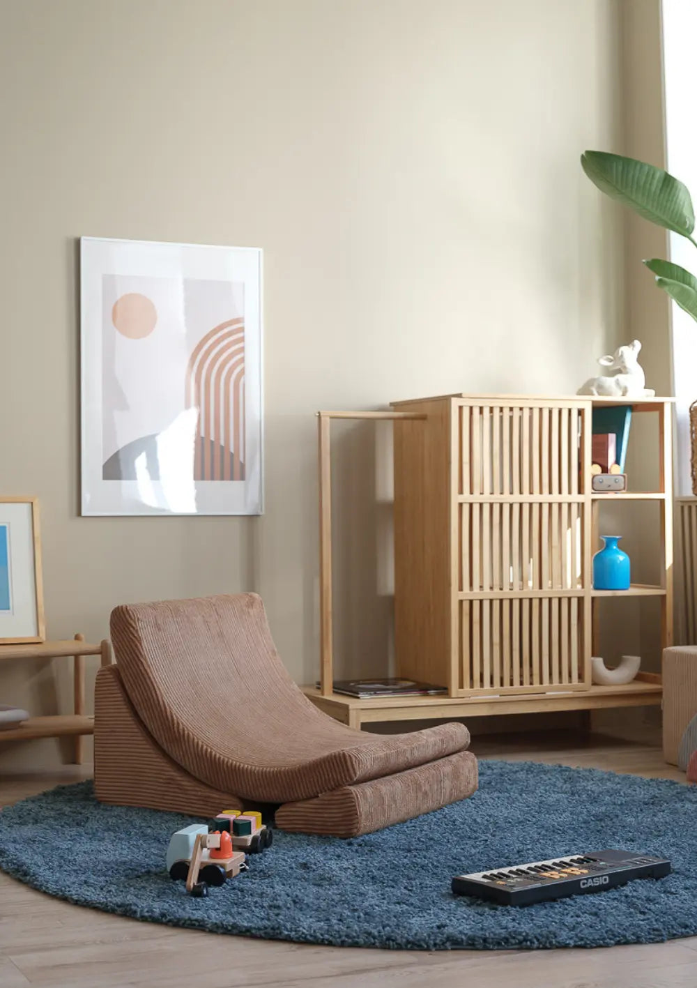 Der braune Wigiwama Kindersessel Moon Chair Cord Toffee aus Breitcord steht frei auf einem blauen Teppich in einem modern eingerichteten Zimmer.