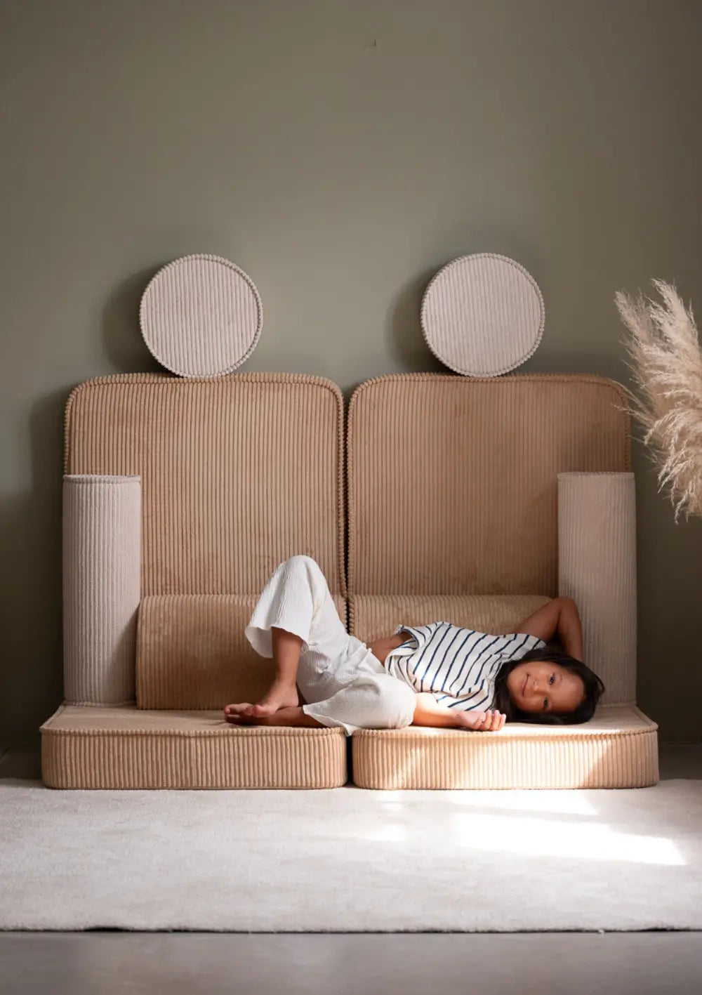 Ein Mädchen liegt entspannt auf der ausgetreckten Spielfläche des modularen Wigiwama Kindersofas Cord Brown Sugar.